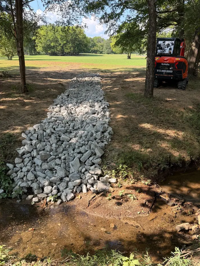 Rock-lined crossing laid across a small creek, excavator behind