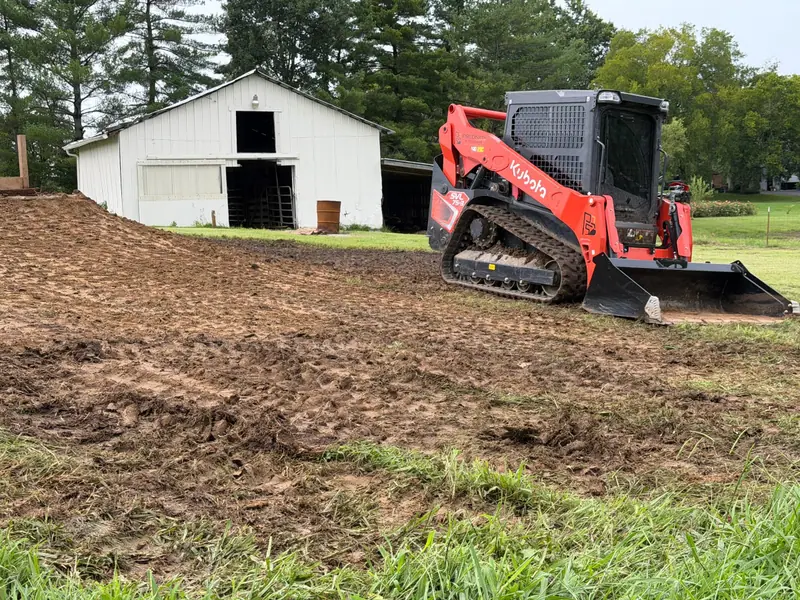 Tracked loader grading beside a white barn